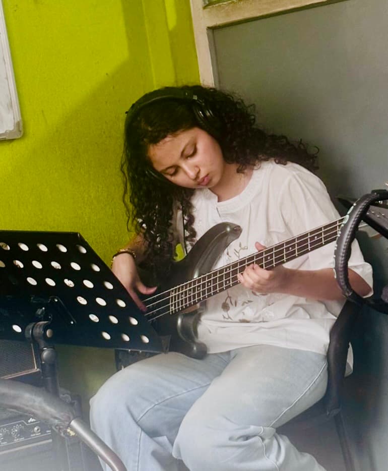 Moulikta smiling while practicing bass guitar with her band