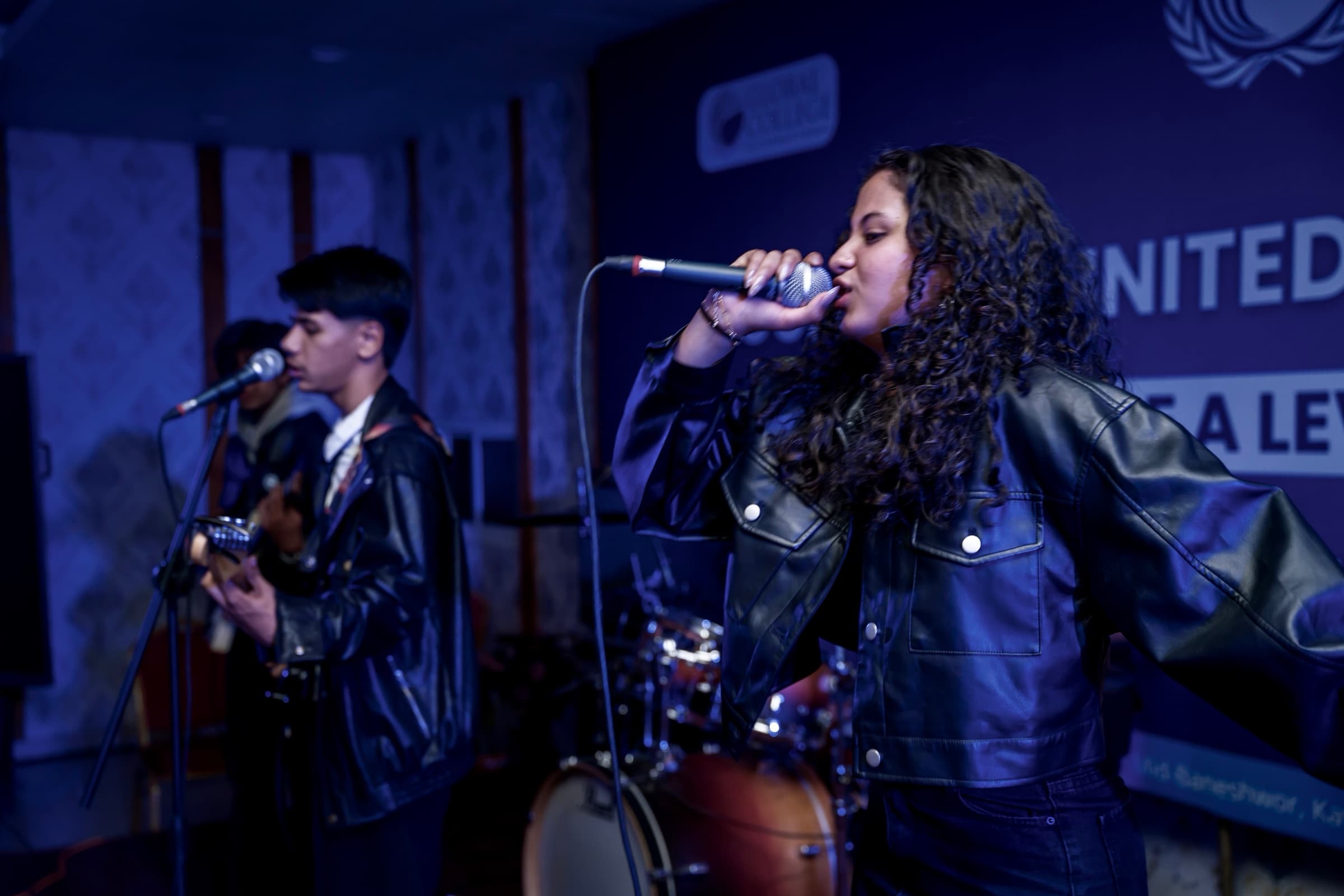 Moulikta singing with a band under blue stage lighting at GCIMUN